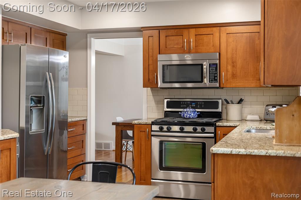 Kitchen with stainless steel appliances, wood finish cabinetry, and light stone countertops