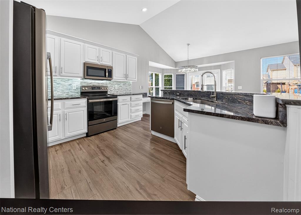Kitchen featuring white cabinets, stainless steel appliances, a chandelier, and lofted ceiling