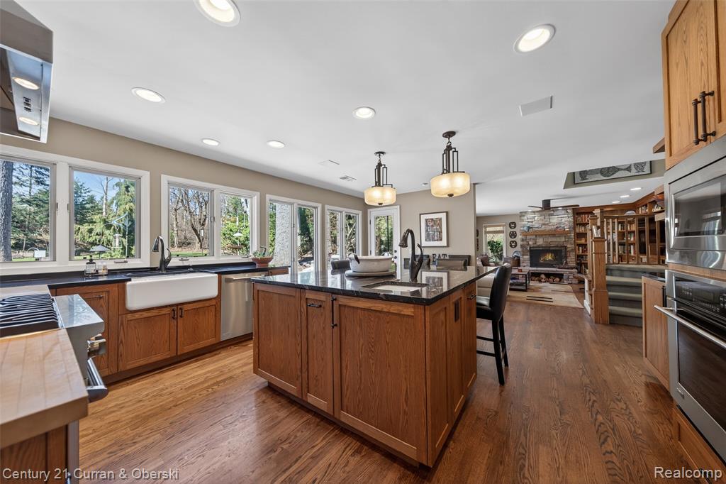 Kitchen featuring wood finish cabinets, stainless steel appliances, an island with sink, hanging light fixtures, and dark wood-type flooring