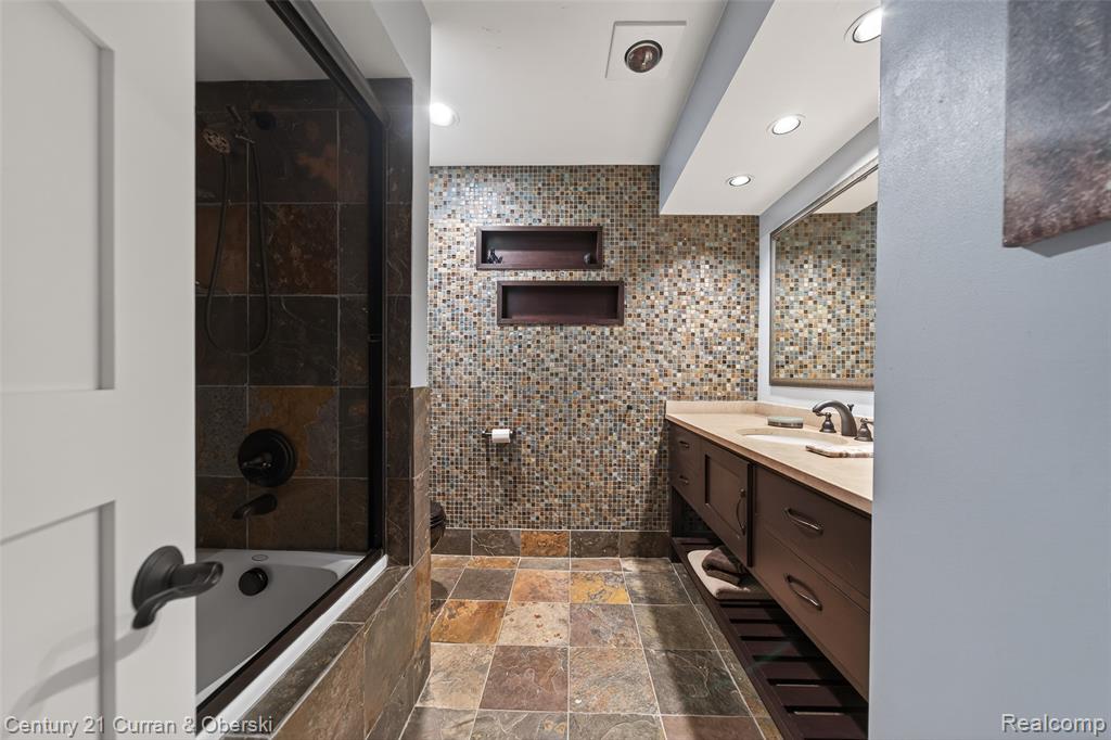 Full bath with vanity, tiled shower / bath, stone tile floors, tile walls, and recessed lighting