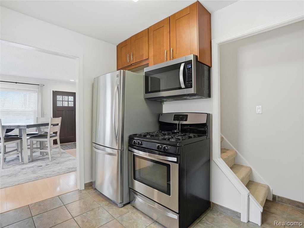 Kitchen with stainless steel appliances, wood finish cabinets, and light tile patterned flooring