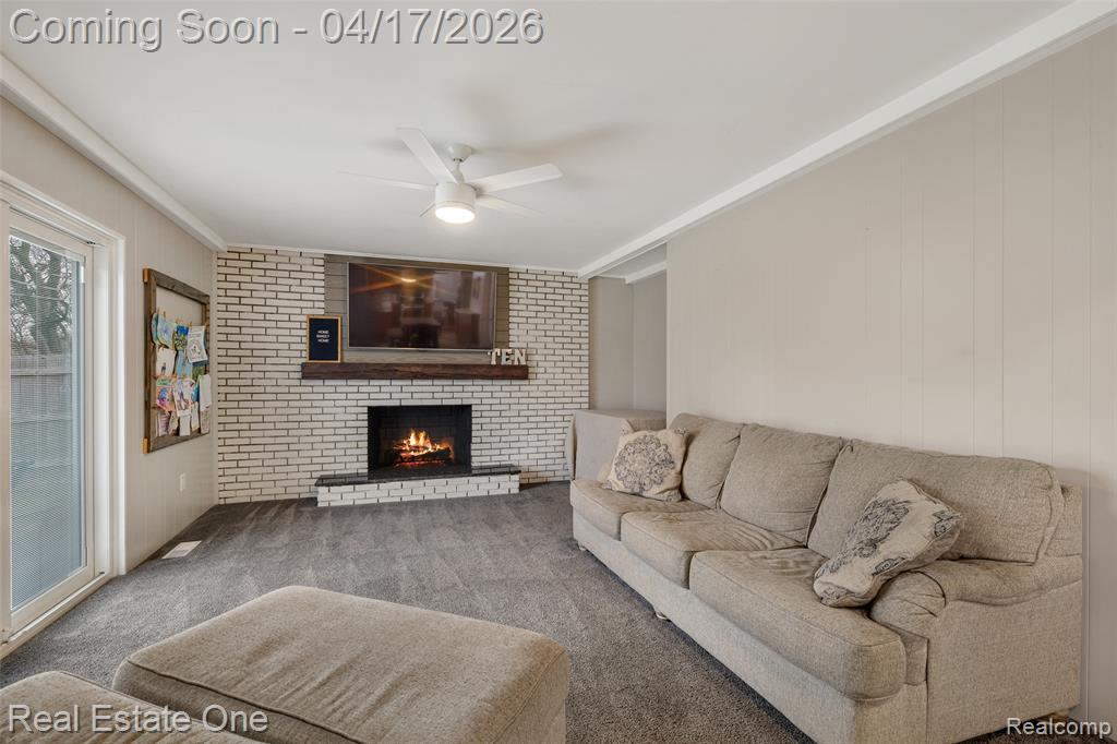 Living room featuring a ceiling fan, ornamental molding, carpet, a fireplace, and wood walls