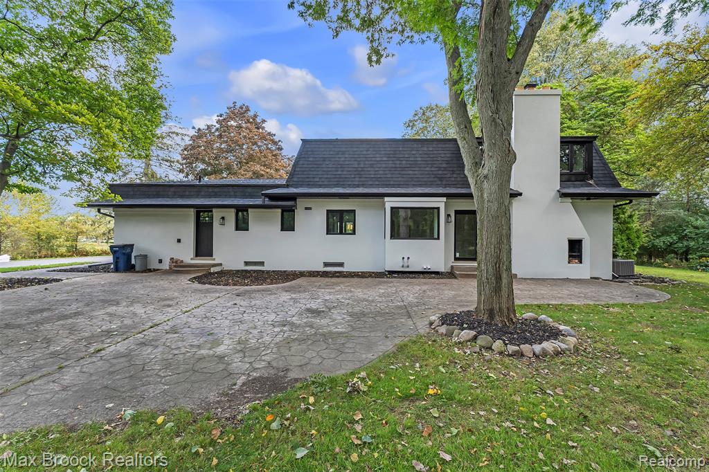 Rear view of property featuring a shingled roof, stucco siding, a patio, a yard, and a chimney