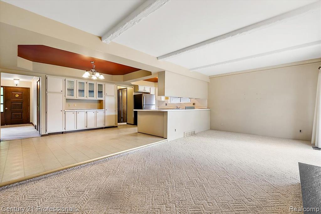 Unfurnished living room with light carpet, a chandelier, beamed ceiling, and a raised ceiling