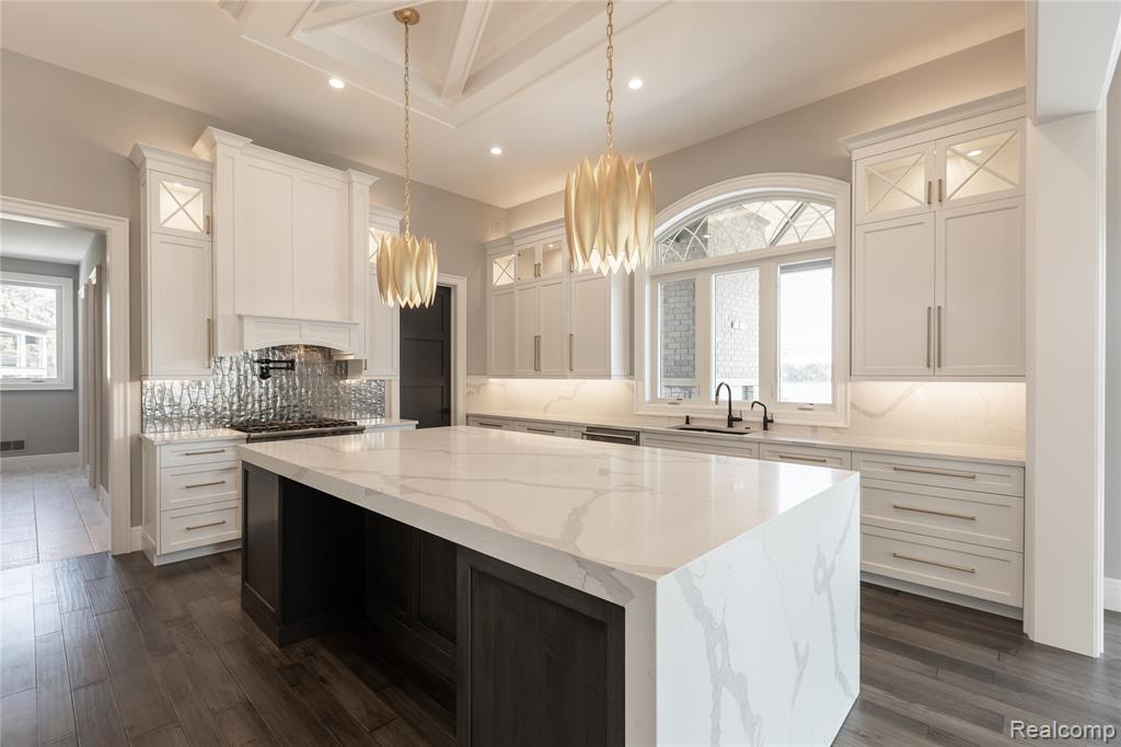 Kitchen with glass insert cabinets, light stone counters, tasteful backsplash, hanging light fixtures, and a kitchen island