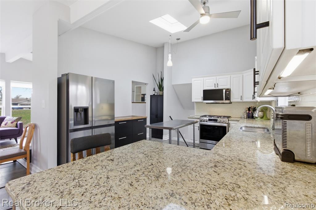 Kitchen with plenty of natural light, stainless steel appliances, white cabinetry, light stone counters, and vaulted ceiling