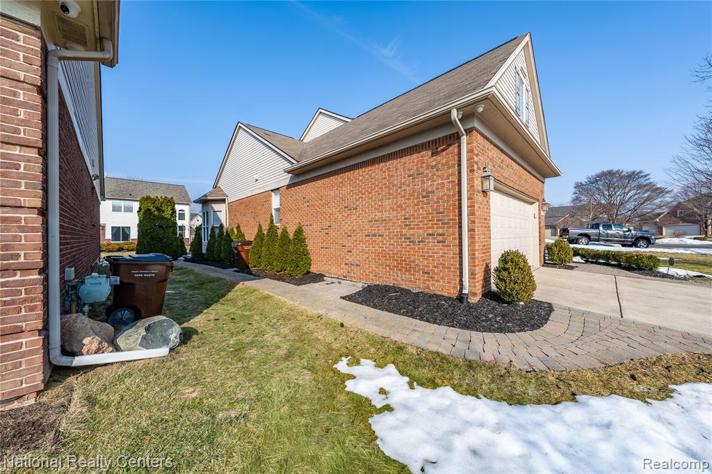 View of property exterior with brick siding, a lawn, concrete driveway, and roof with shingles