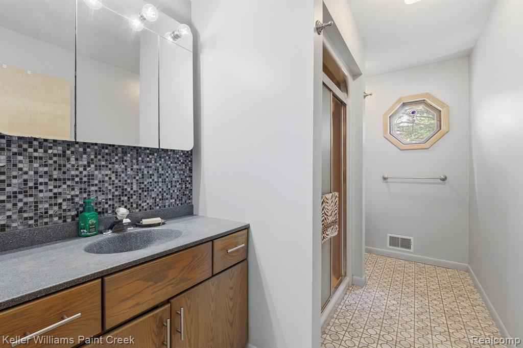 Bathroom featuring a vanity with an integrated sink, mosaic tile backsplash, wood-finish cabinetry, and a walk-in shower with a glass enclosure