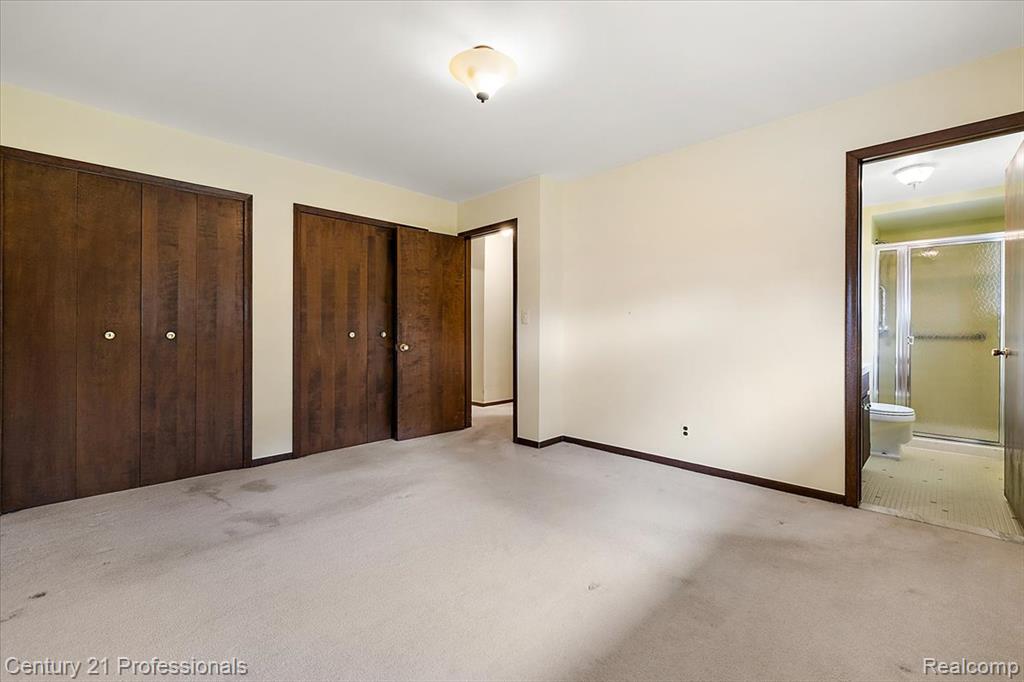 Unfurnished bedroom featuring multiple closets, ensuite bathroom, and light carpet