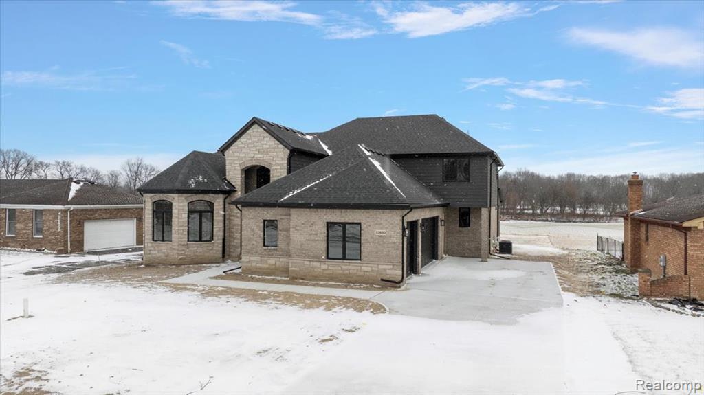 French country inspired facade with brick siding, stone siding, and a garage