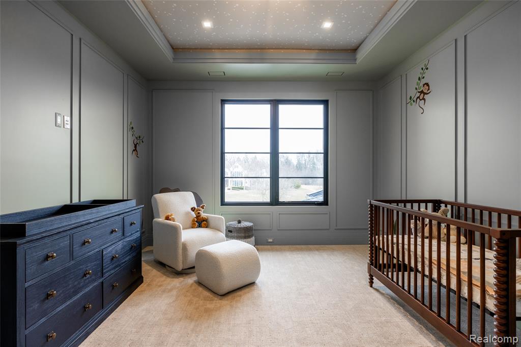 Bedroom featuring a nursery area, a decorative wall, a tray ceiling, light carpet, and ornamental molding