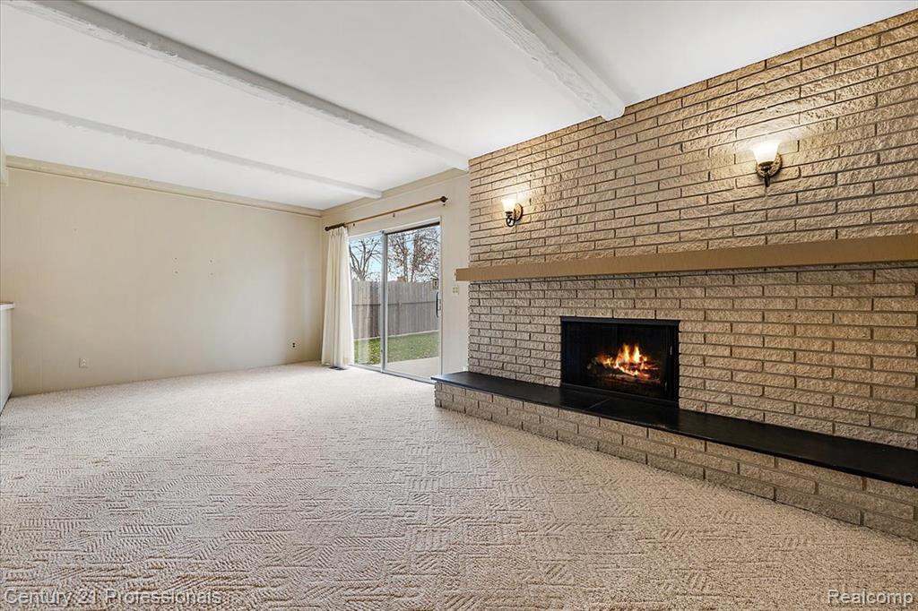 Unfurnished living room with a brick fireplace, beamed ceiling, carpet flooring, and brick wall