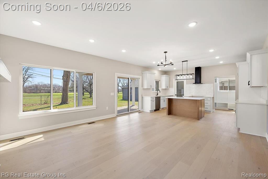 Kitchen featuring two tone color scheme, light countertops, a kitchen island, open floor plan, and decorative light fixtures