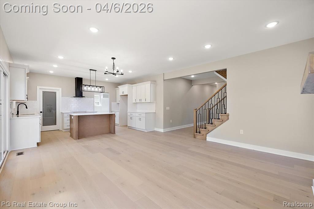 Two tone kitchen featuring open floor plan, two tone color scheme, ventilation hood, a kitchen island, and a chandelier