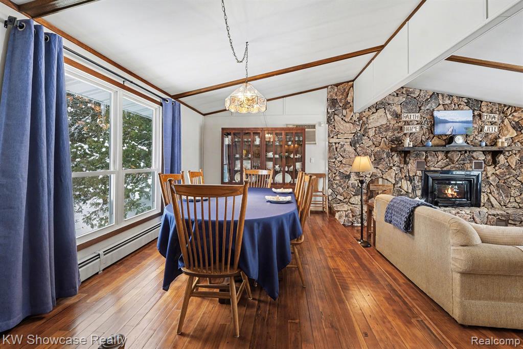 Dining room with a fireplace, hardwood / wood-style flooring, a baseboard heating unit, and vaulted ceiling with beams
