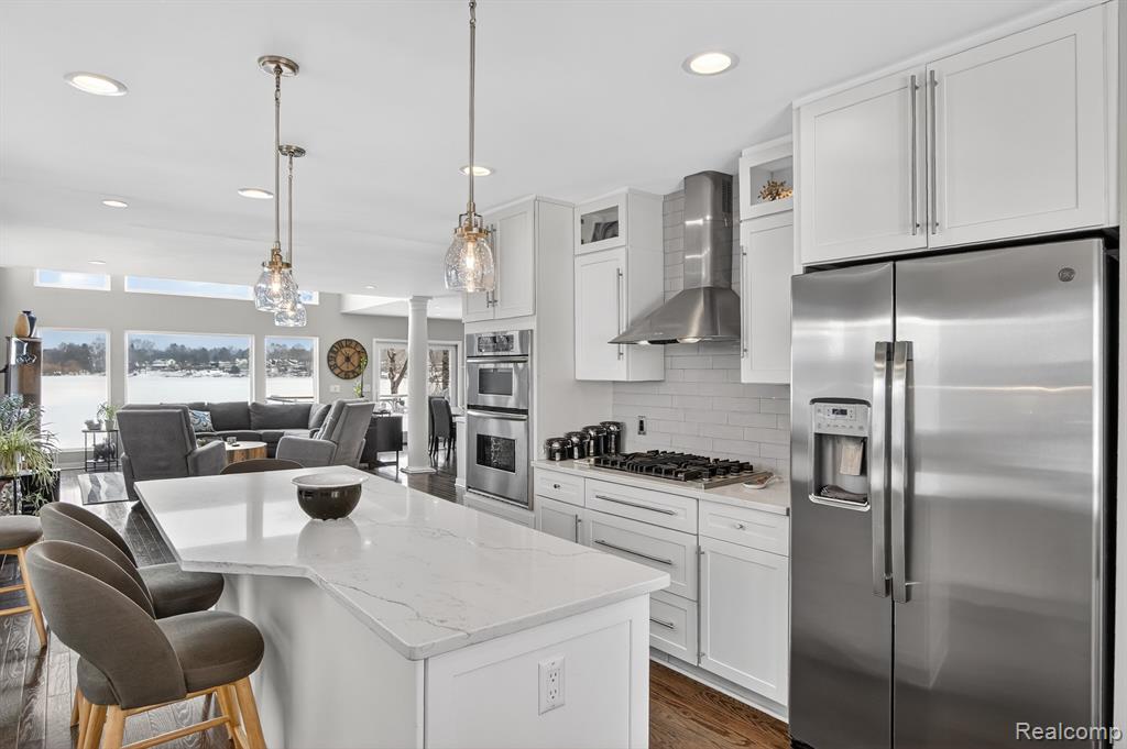 Kitchen with dark wood finished floors, glass insert cabinets, stainless steel appliances, wall chimney exhaust hood, and recessed lighting