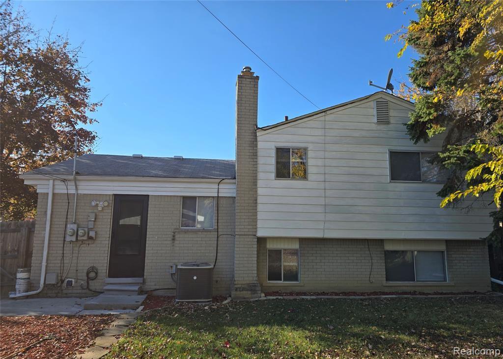 Back of house featuring brick siding, a chimney, a lawn, and entry steps