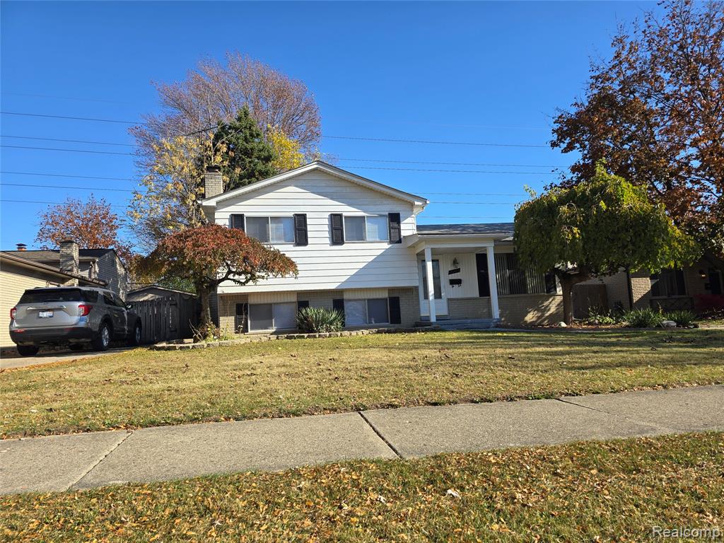 Split level home with a front lawn, a porch, a chimney, and brick siding
