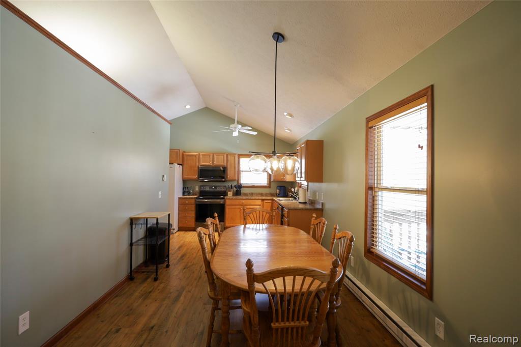 Dining room with baseboard heating, dark wood-type flooring, vaulted ceiling, and a ceiling fan
