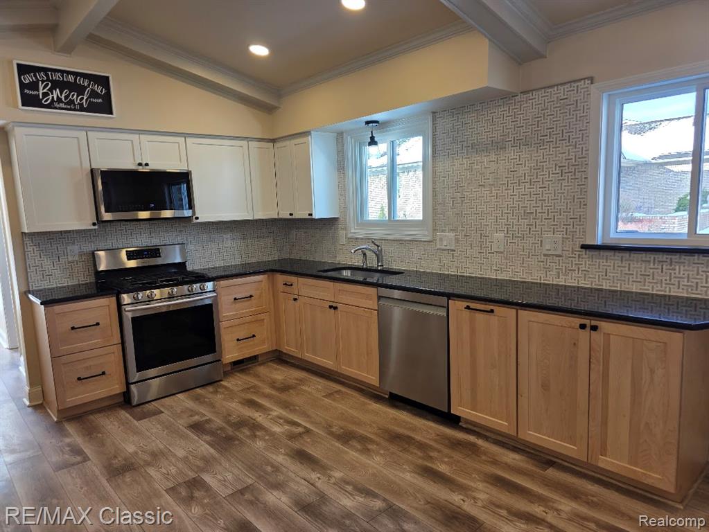 Kitchen with stainless steel appliances, crown molding, decorative backsplash, dark wood-style floors, and dark stone countertops