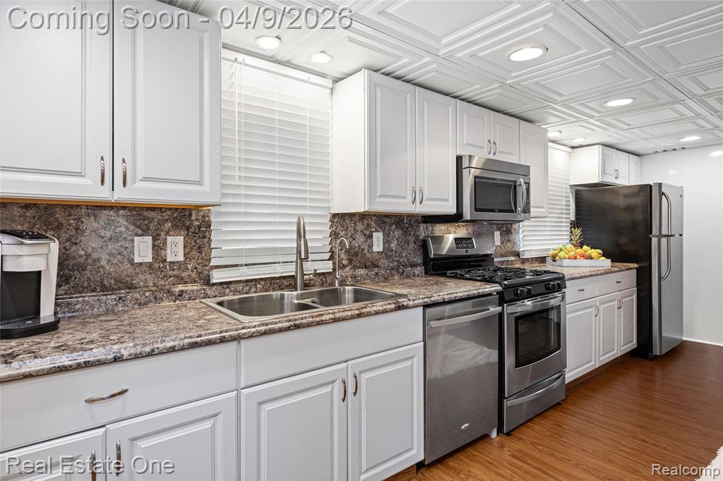 Kitchen with white cabinets, stainless steel appliances, wood finished floors, tasteful backsplash, and recessed lighting