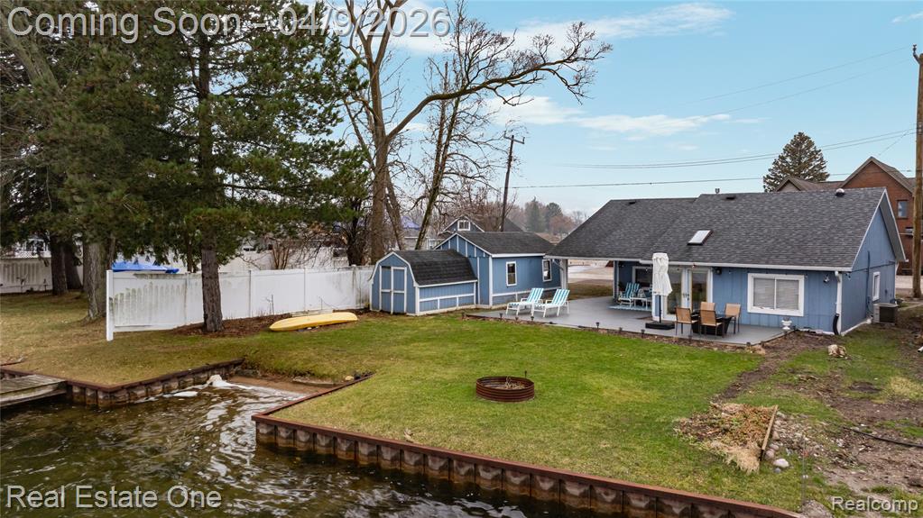 Rear view of property with an outdoor fire pit, a patio area, a fenced backyard, a shingled roof, and a storage unit