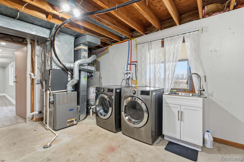Laundry area featuring unfinished concrete flooring, heating unit, washer and clothes dryer, and water heater