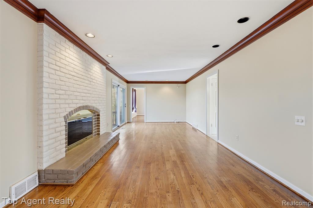 Unfurnished living room with a brick fireplace, ornamental molding, light wood finished floors, and recessed lighting