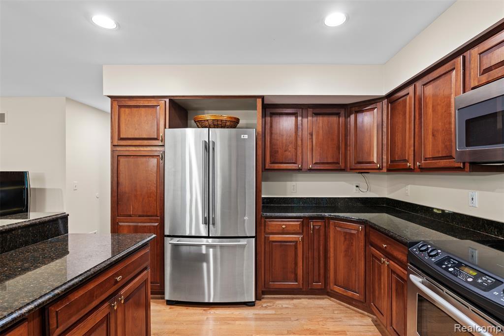Kitchen featuring appliances with stainless steel finishes, dark stone countertops, light wood finished floors, and recessed lighting