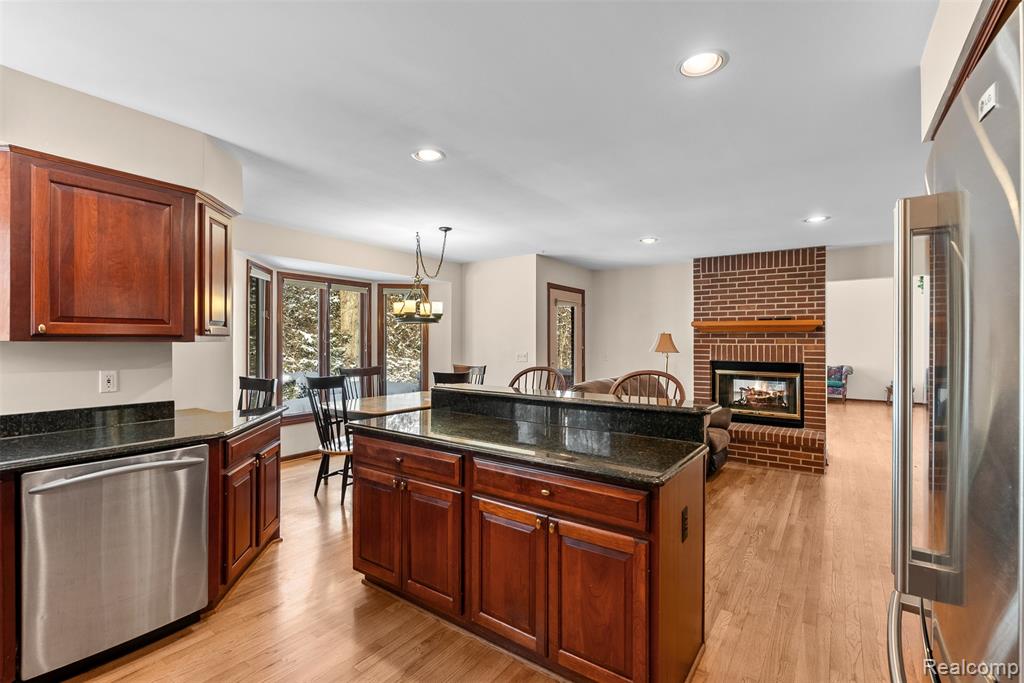 Kitchen featuring dark stone countertops, appliances with stainless steel finishes, pendant lighting, a brick fireplace, and light wood-type flooring