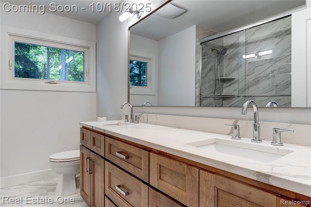 Bathroom featuring a marble finish shower, double vanity, and light marble finish floors