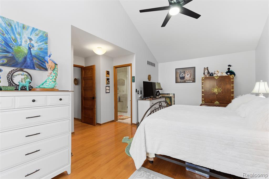 Bedroom with vaulted ceiling, ceiling fan, light wood finished floors, and ensuite bathroom
