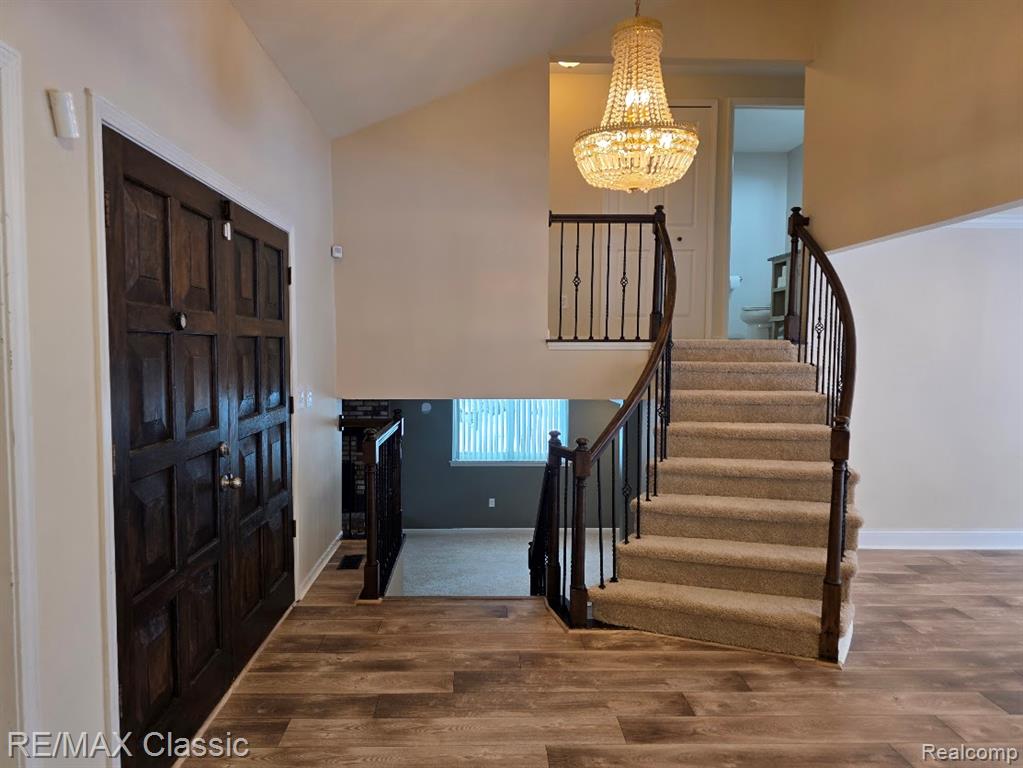 Entrance foyer featuring vaulted ceiling, wood finished floors, a chandelier, and stairs