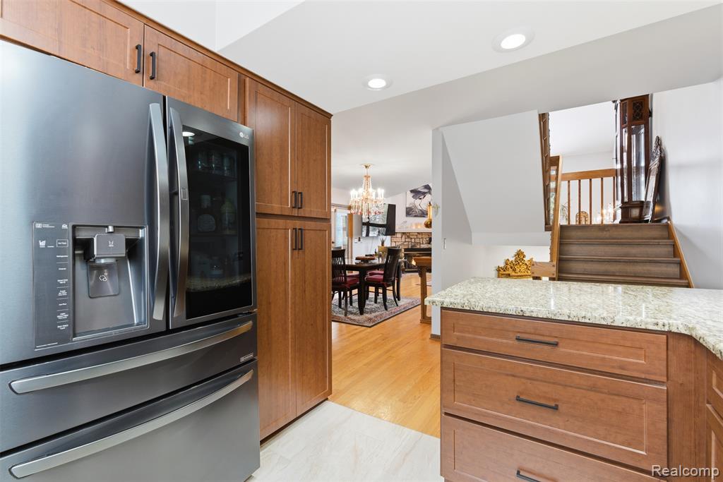 Kitchen with stainless steel fridge with ice dispenser, wood finish cabinets, light stone countertops, and suspended lighting