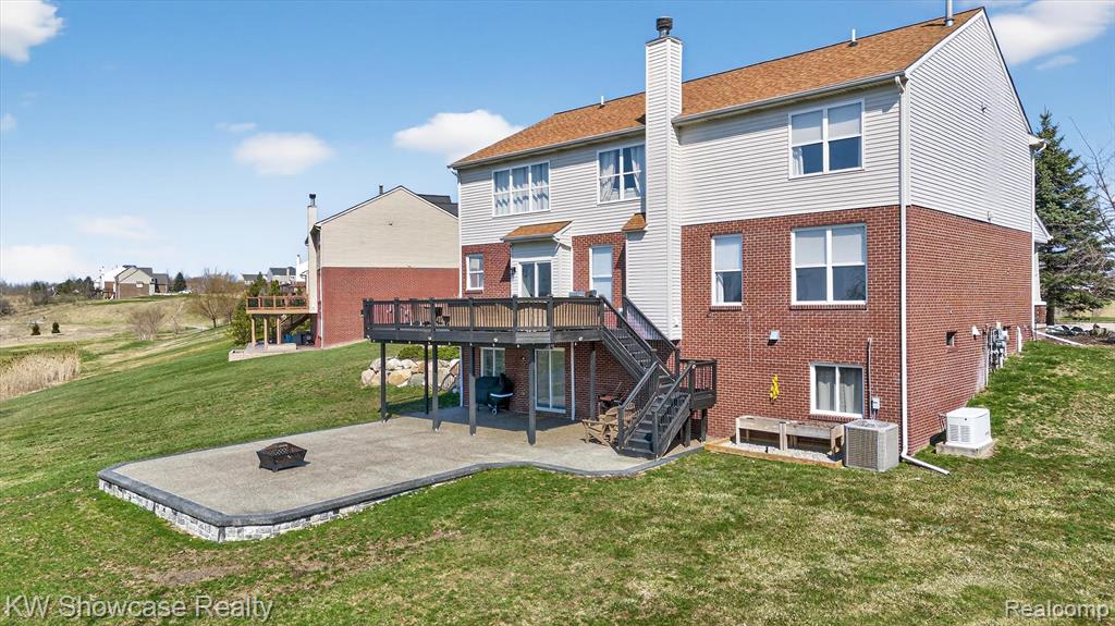 Rear view of house featuring a patio, an outdoor fire pit, a wooden deck, a yard, and a chimney