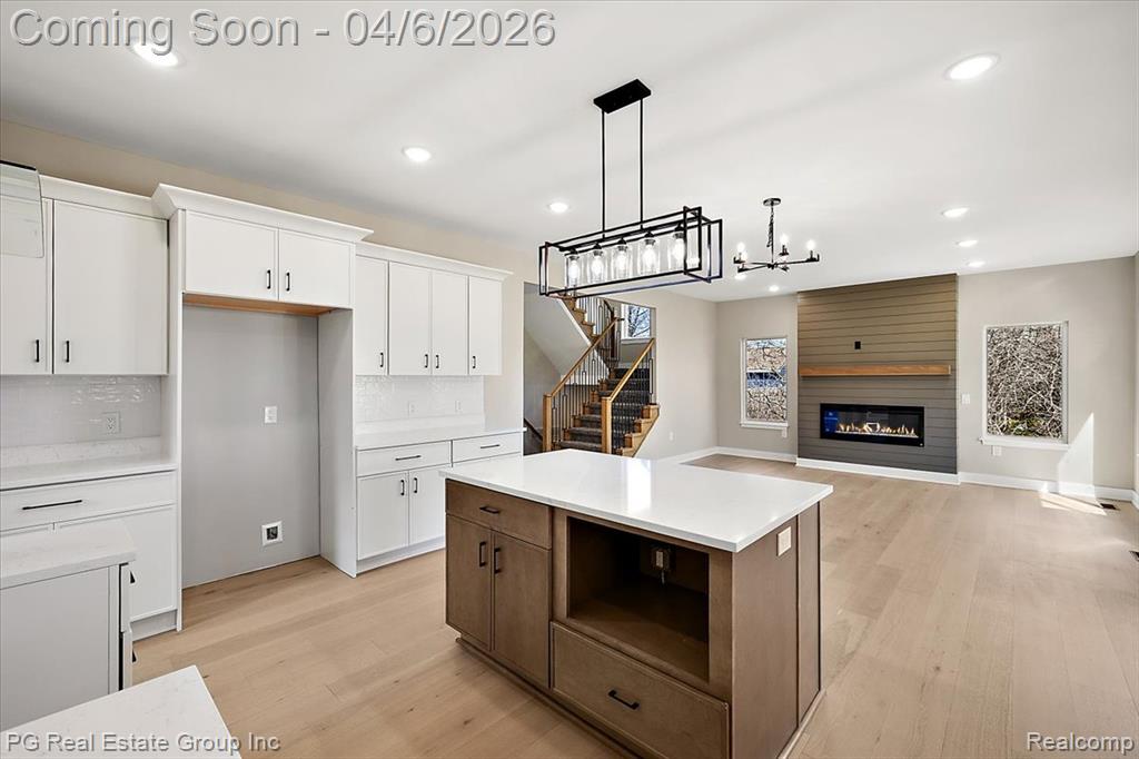 Kitchen featuring open floor plan, suspended lighting, light wood-style floors, a large fireplace, and backsplash