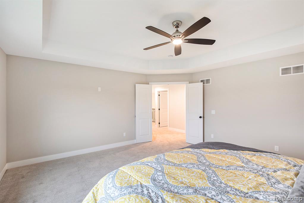 Bedroom featuring light carpet, a ceiling fan, and a tray ceiling