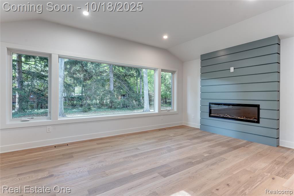 Unfurnished living room with vaulted ceiling, wood finished floors, recessed lighting, and a fireplace