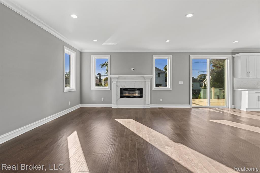 Unfurnished living room with crown molding, dark wood-type flooring, a high end fireplace, and recessed lighting