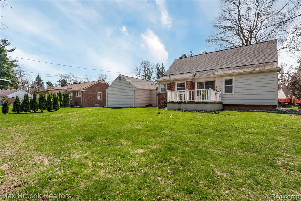 Back of property with a yard, roof with shingles, and a wooden deck