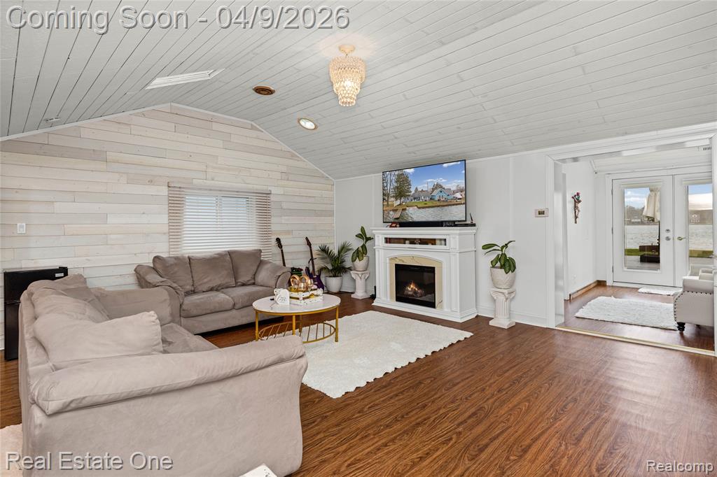 Living area with wooden walls, dark wood-style flooring, a lit fireplace, and wooden ceiling