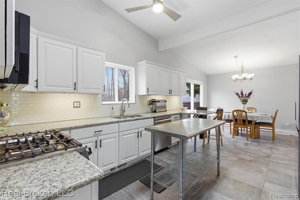 Kitchen featuring white cabinetry, light stone countertops, dishwasher, ceiling fan, and vaulted ceiling