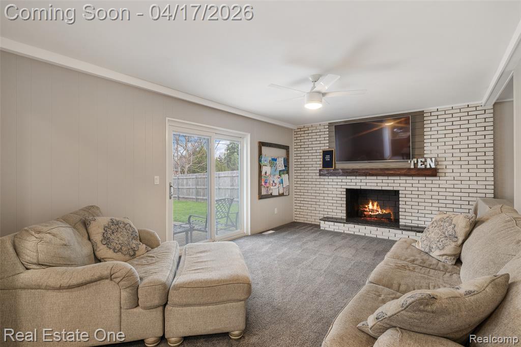 Carpeted living room featuring a ceiling fan, a brick fireplace, and crown molding