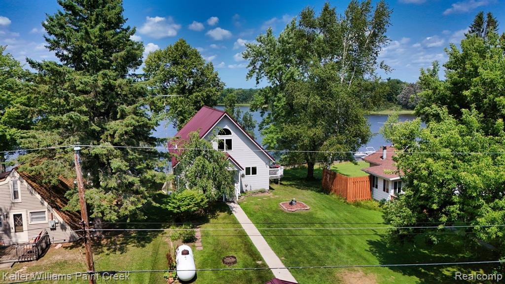 Waterfront property with a red-toned metal roof, white siding, and a prominent gable window