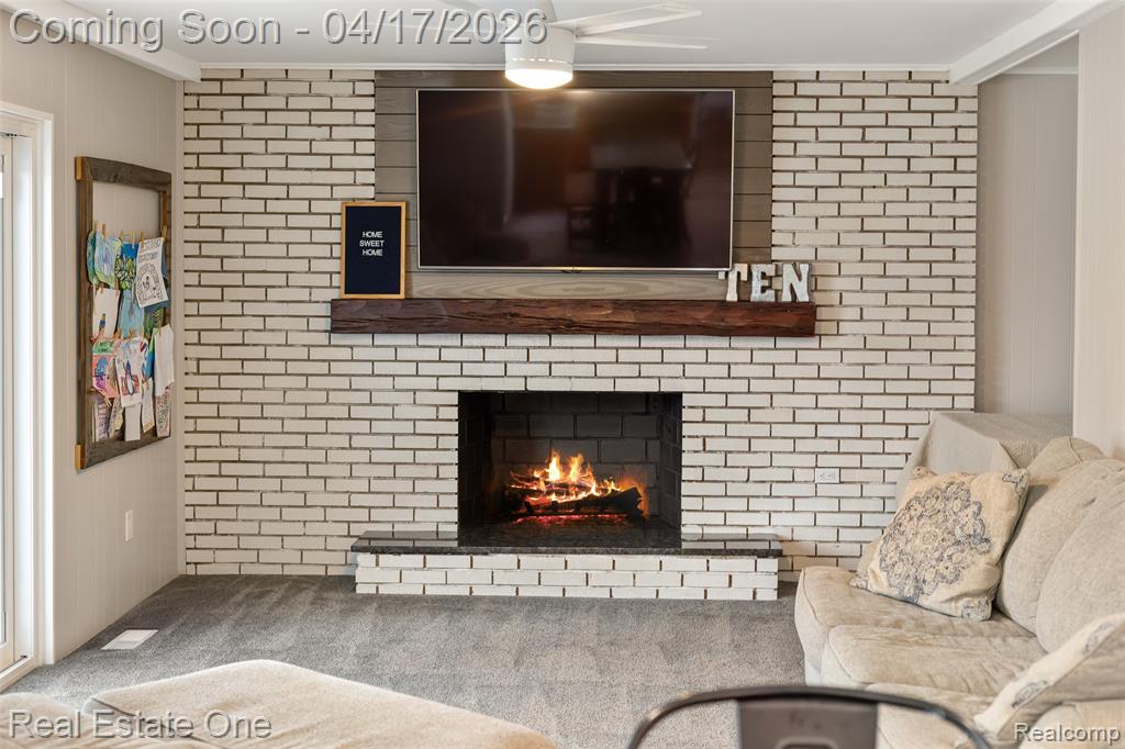 Living room featuring carpet floors, wooden walls, and a brick fireplace