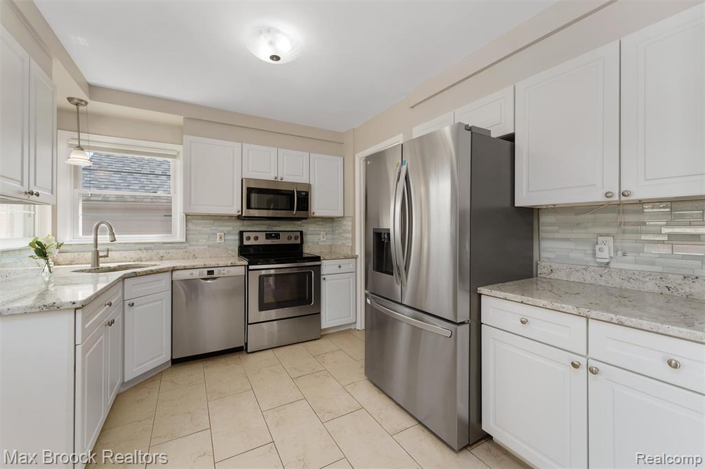 Kitchen with stainless steel appliances, white cabinets, light stone countertops, and decorative backsplash