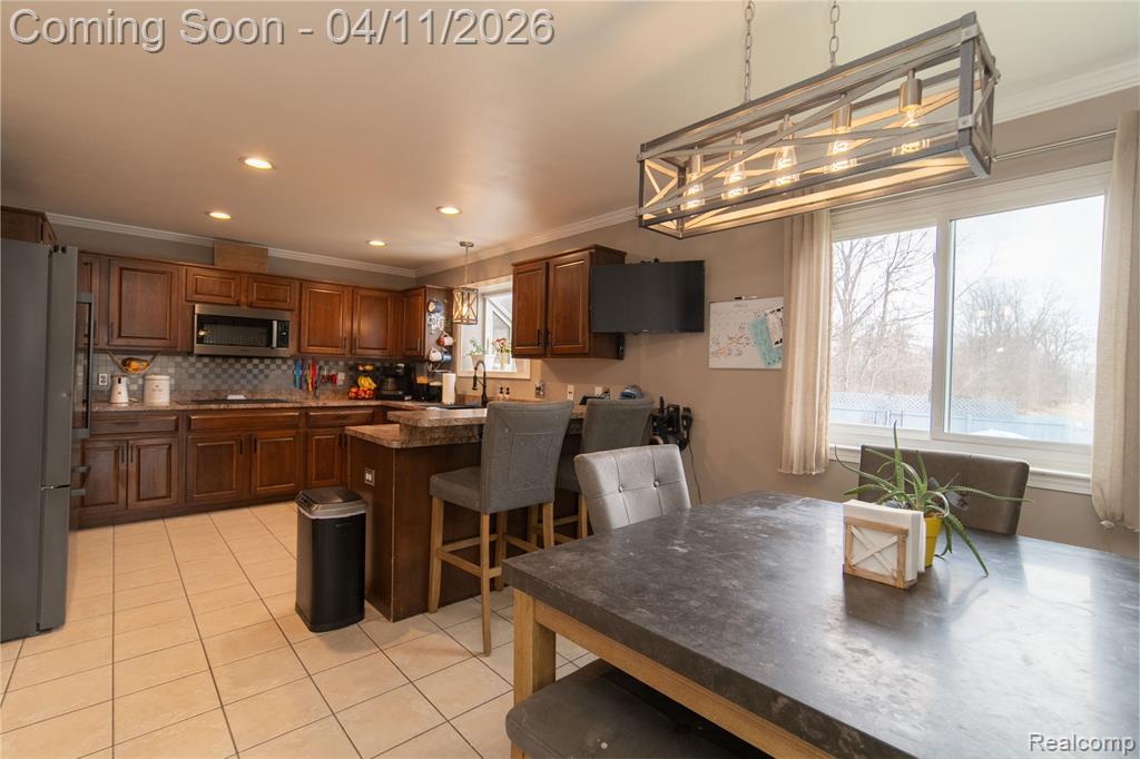 Kitchen with crown molding, a breakfast bar, stainless steel appliances, hanging light fixtures, and light tile patterned floors