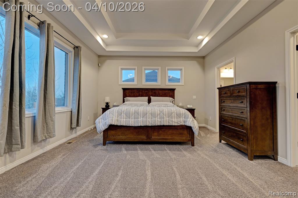 Bedroom with light carpet, recessed lighting, multiple windows, and a raised ceiling