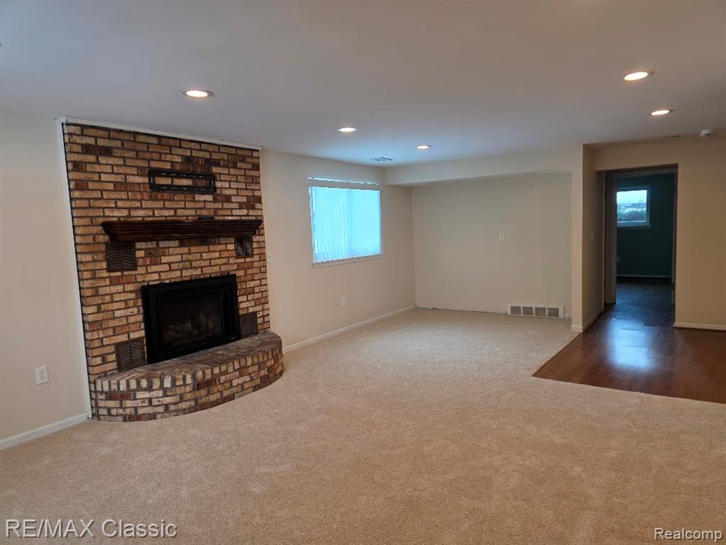 Unfurnished living room featuring carpet floors, a brick fireplace, and recessed lighting