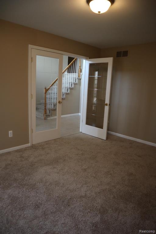 Unfurnished room with stairs, french doors, and light carpet